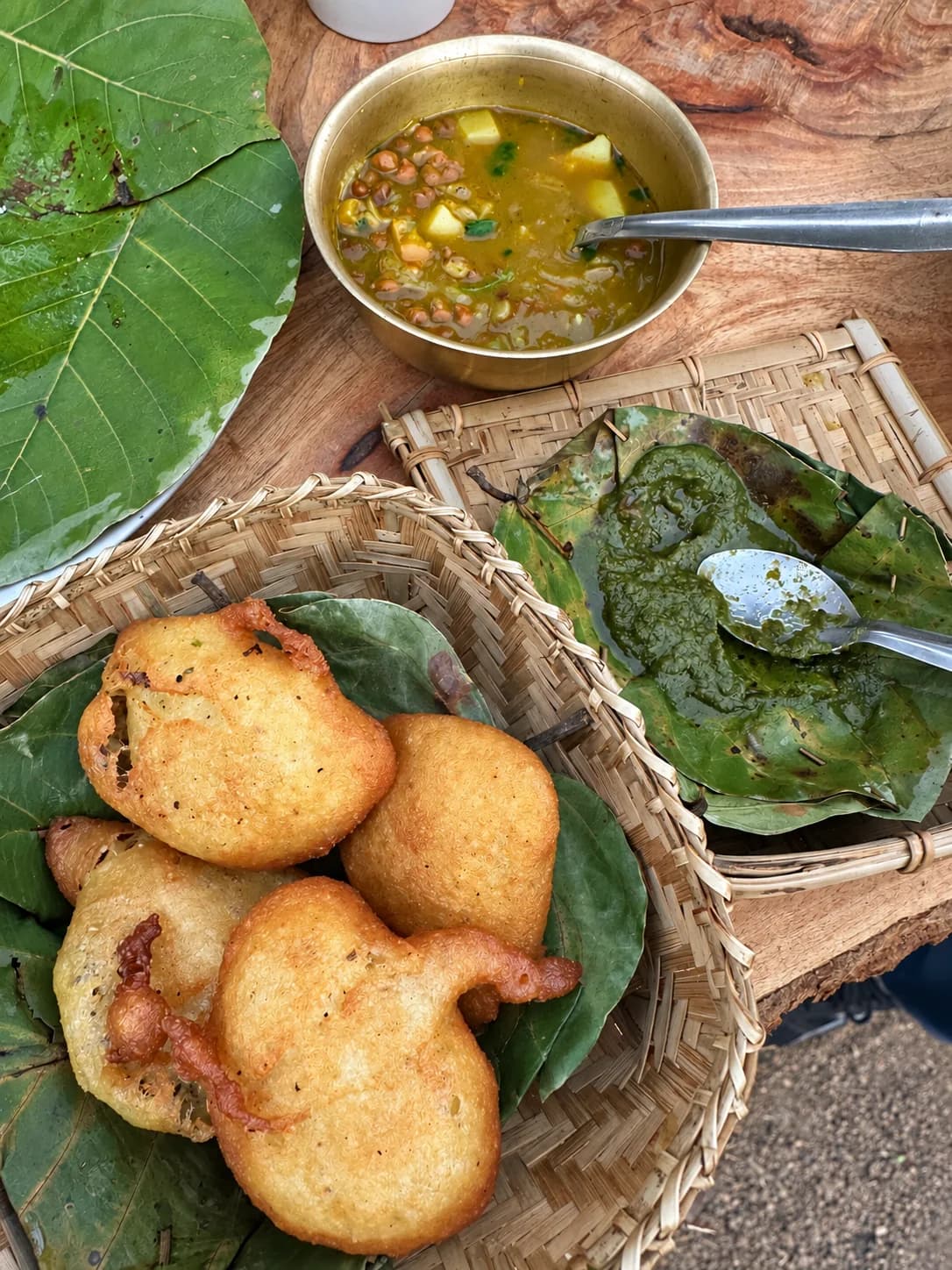 Golden food in a leaf-lined basket beside a brass bowl and green accompaniment at Ajam Emba