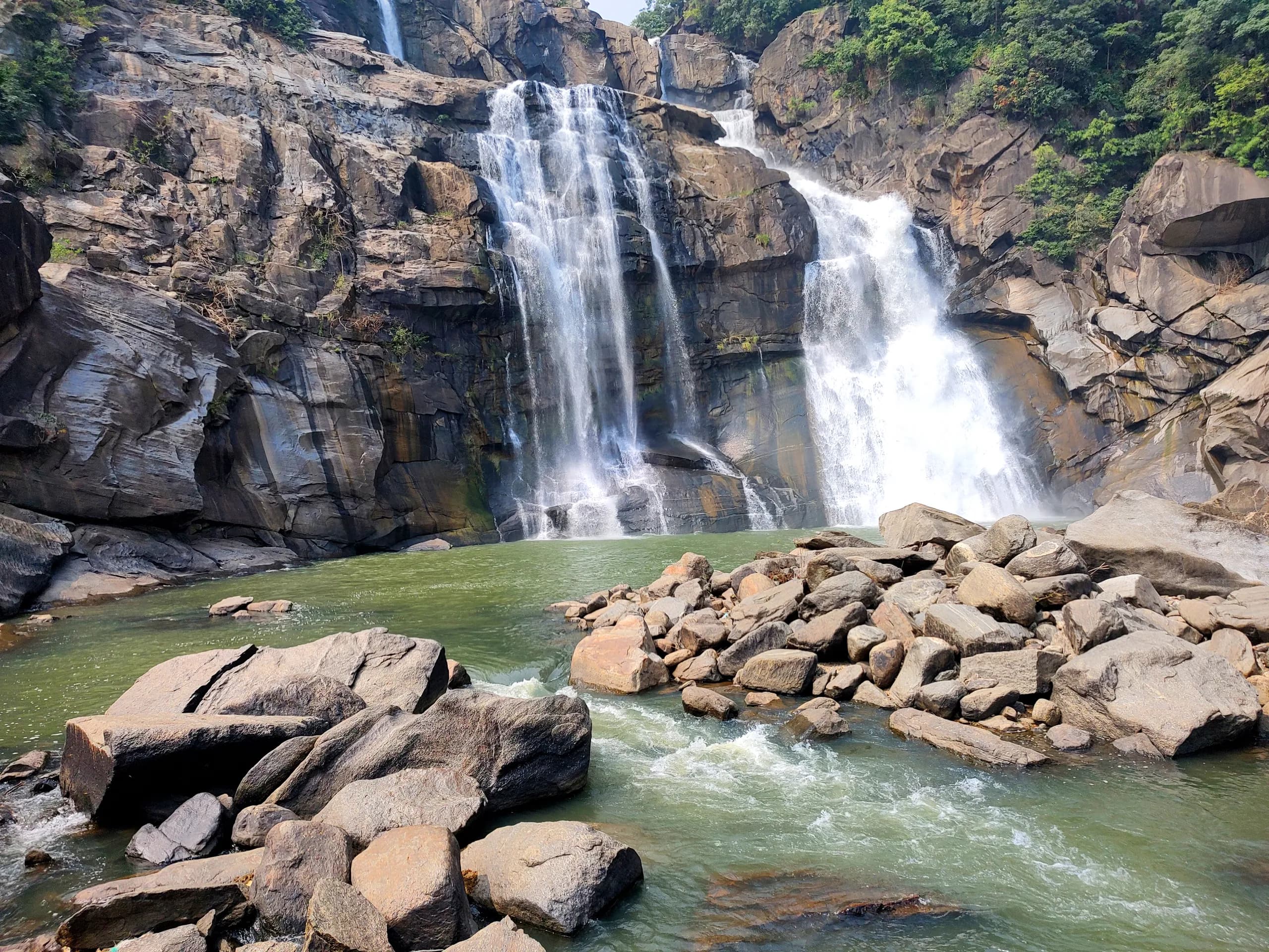 Hundru Falls descending over layered rock into a pool edged with large boulders