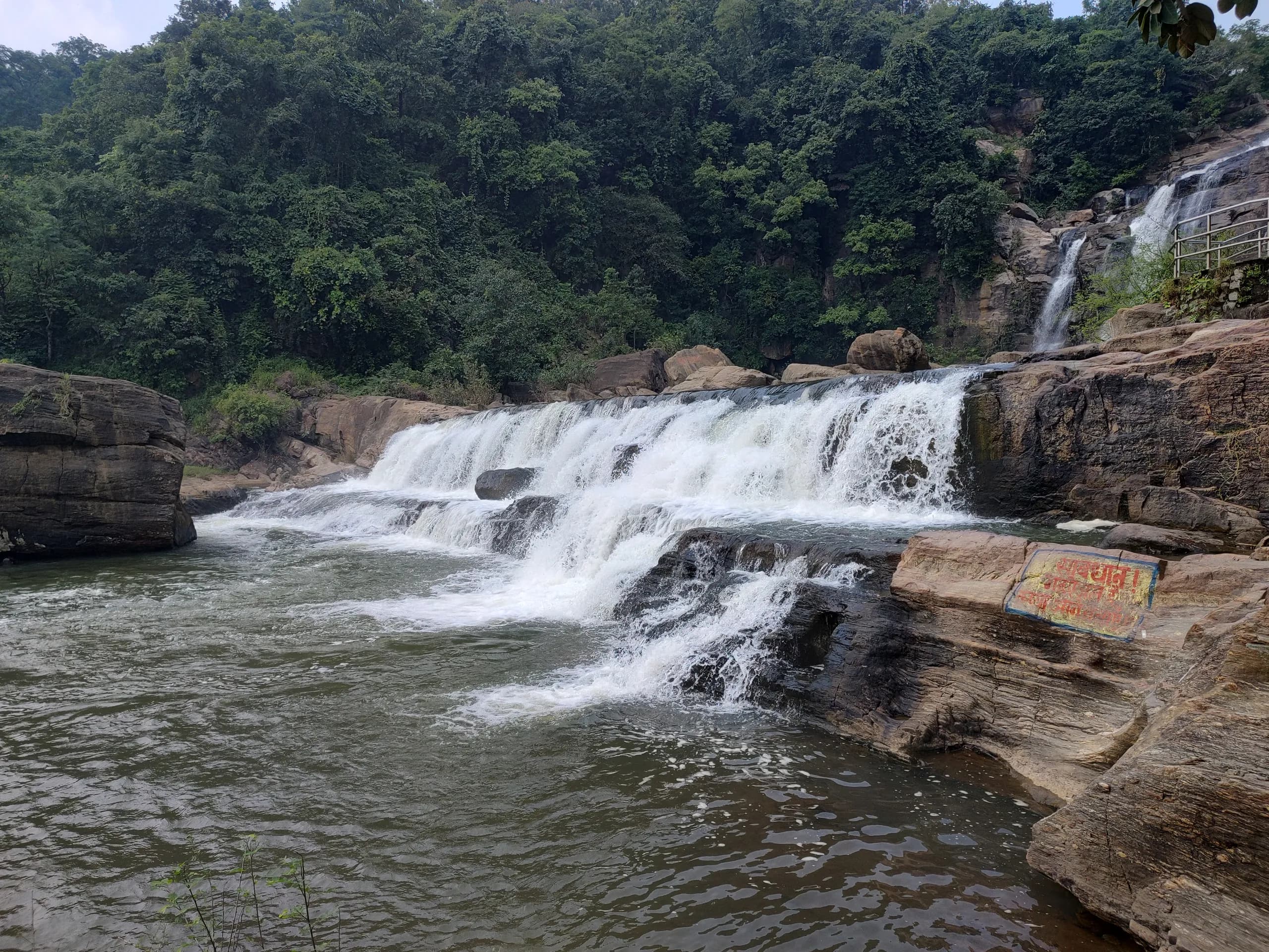Jonha Falls cascading over broad rock shelves with forest along the far bank